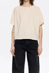 Remera color crema de corte holgado y mangas cortas con detalle de pinzas en los hombros.