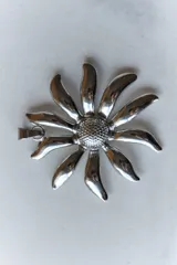 Collar con tiento negro y dije plateado en forma de flor con centro texturizado.