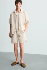 Bermuda regular fit color beige con bordados de flores en tono marrón. Tiene cintura elástica ajustable con cordón, bolsillos laterales y un bolsillo trasero de plastrón.