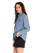 Camisa de manga larga celeste de denim con dos bolsillos en el pecho y cierre con botones metálicos.