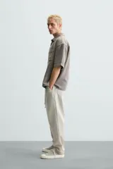 Pantalón color arena de corte recto, confeccionado en tejido de algodón y lino. Cuenta con cintura elástica ajustable con cordón, bolsillos delanteros y traseros de parche.