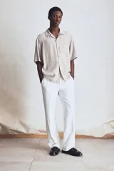 Camisa de manga corta color beige con cuello abierto, tapeta lisa, bolsillo superior y bajo recto. Corte estándar para una silueta clásica y cómoda.