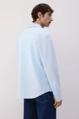 Camisa celeste de lino y algodón, corte regular, manga larga, cuello inglés, bolsillo en el pecho y cierre con botones.