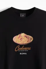 Remera negra de corte holgado con estampado de un plato de pasta carbonara y texto en color ocre.