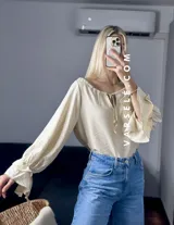 Blusa blanca de mangas largas con volados en los puños y escote con lazo.