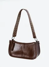 Cartera baguette marrón de cuero sintético con tachas plateadas en el asa. Tiene cierre superior y herrajes plateados.