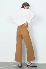 Pantalón de jean de tiro alto color negro con pierna ancha, bolsillos delanteros y traseros, y cierre frontal con cremallera y botón metálico.