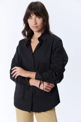 Camisa negra de manga larga con cuello clásico y cierre frontal con botones. Las mangas tienen frunces y lazos para ajustar el largo.