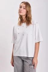 Remera blanca de corte holgado con mangas cortas y detalle de ojalillos metálicos en el frente.