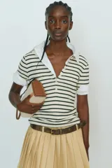 Remera polo entallada en punto acanalado a rayas horizontales negras y crudas, con cuello clásico y tapeta de botones.