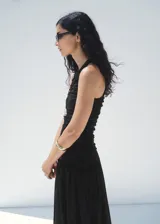 Vestido midi negro sin mangas, con cuello redondo, fruncidos laterales y diseño evasé.