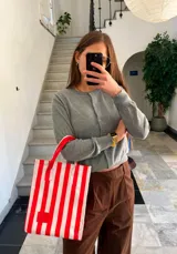 Bolso tipo shopper de tela blanca con rayas verticales rojas y asas rojas.