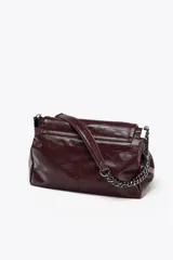 Bolso de hombro marrón oscuro de cuero sintético, con solapa y cierre magnético. Tiene un asa de cadena plateada y tres compartimentos internos, uno de ellos con cierre de cremallera.