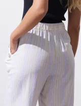 Pantalón capri de lino color blanco con rayas verticales celestes y amarillas, pretina elastizada, bolsillos delanteros y botones decorativos.