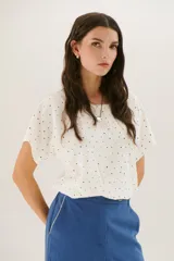 Blusa color crema con estampado de lunares negros, cuello redondo y mangas cortas.