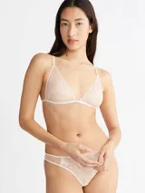 Conjunto de lencería color rosa pálido, compuesto por un corpiño triangular de encaje floral sin aro ni relleno, con tirantes finos regulables y cierre frontal metálico, y una bombacha tipo tanga de encaje floral con laterales de tul.