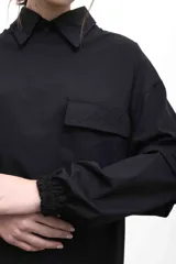 Remerón negro oversize con cuello camisero gris, mangas largas grises con puños elásticos, bolsillo con tapa en el pecho y logo bordado.