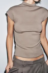Top sin mangas, color marrón topo, con cuello alto y corte recto. Presenta un tejido de punto fino y mangas sisa con caída.
