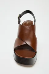 Sandalias de cuero color marrón con plataforma y tacón cuadrado. Tiras cruzadas en la parte delantera y cierre mediante tira trasera con hebilla lateral.