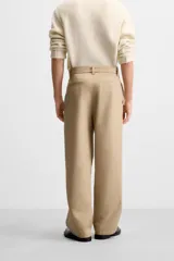 Pantalón negro de corte ancho con cinturón de tela con hebilla metálica y pliegues frontales.