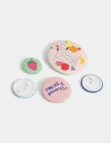 Set de cinco pins con diferentes diseños estampados de frutas y frases.
