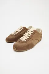 Zapatillas deportivas color marrón de piel con detalle de pespuntes, suela dentada, forro interior y parte trasera en contraste color crema. Cierre con cordones y acabado en punta redonda.