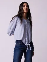 Blusa de algodón a rayas verticales azules y blancas, con cuello en V, mangas 3/4 y cierre frontal con botones. Tiene un nudo en la parte delantera.