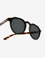 Lentes de sol Hawkers unisex, modelo Warwick, con montura redonda negra y patillas Carey.