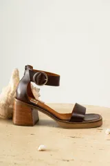 Sandalias de cuero color crudo, con tira ancha sobre los dedos, pulsera con hebilla al tobillo y taco cuadrado de madera.