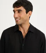 Camisa negra de lino con corte clásico, cuello camisero y mangas largas. Cierre frontal con botones.