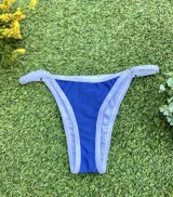 Bikini de dos piezas color azul eléctrico con ribete blanco. El corpiño es de estilo triángulo con tirantes finos regulables y la bombacha es colaless regulable con tiras laterales finas.