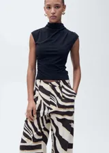 Pantalón de mujer con estampado de cebra en tonos blanco, negro y dorado. Diseño wide leg, tiro medio, con trabillas, pinzas y dos bolsillos laterales. Cierre delantero con botón, gancho y cremallera ocultos.