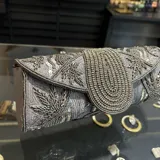 Sobre de fiesta color gris con bordado artesanal de mostacillas y lentejuelas plateadas. Tiene asa de cadena plateada para colgar al hombro.