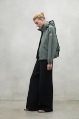 Campera color crema de corte oversize con capucha ajustable, cierre frontal con botones a presión y bolsillos laterales con solapa. Fabricada con poliamida reciclada, impermeable y transpirable.