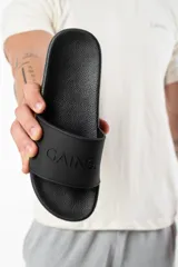 Chanclas negras con la palabra "GAIN" en relieve en la tira superior y "AMBITION" en el lateral de la suela.