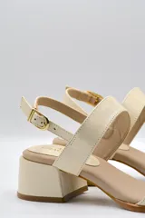Sandalias de cuero color beige con taco cuadrado y tira ancha sobre los dedos. Presenta pulsera al tobillo con hebilla dorada.