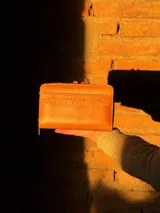 Billetera rectangular de cuero color naranja con cierre de cremallera y diseño geométrico en relieve.