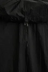 Cazadora negra de tejido técnico ripstop, con cuello alto, capucha ajustable y visera. Tiene mangas largas con puños elásticos, bolsillo de seguridad con cremallera en el pecho, bajo con elástico en los laterales y cierre frontal con cremallera.