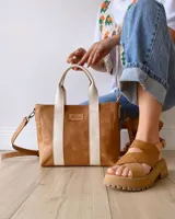Bolso tipo tote de cuero color camel con dos tiras verticales blancas y correa larga ajustable al hombro.
