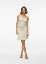 Pollera corta tejida color beige claro, con pretina ajustable mediante cordón y terminación con volado en el ruedo. Presenta un tejido de punto abierto.