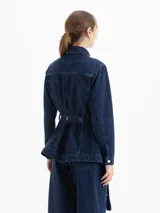 Parka larga de denim azul oscuro, con cuello camisero, bolsillos delanteros con tapa y cinturón ajustable con arandelas metálicas.