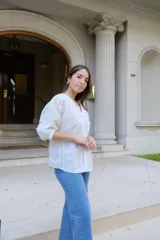 Blusa blanca de manga larga con elástico en puños, escote en pico y cierre frontal con botones. Detalles de bordados con hilado en tonalidad camel y acabado con entredoses a tono.