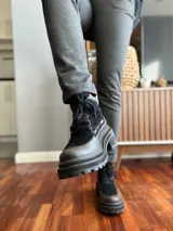 Borcego de cuero negro con puntera redondeada, cordones negros, paneles laterales de gamuza negra y detalle de cuero texturizado en el tobillo. Suela track de goma negra.