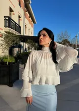 Blusa color blanco hueso, de cuello alto con volados, mangas largas acampanadas con volados y corte crop.