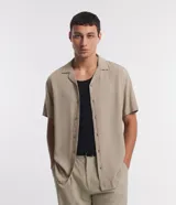 Camisa boxy masculina de viscosa color beige, con mangas cortas, cuello camisero y abotonadura frontal.
