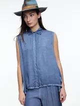 Camisa celeste sin mangas confeccionada en viscosa teñida en frío, con efecto gastado. Con cuello clásico y cartera oculta. El ruedo irregular, más largo en los laterales, aporta movimiento y una silueta original.