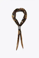 Pañuelo bandana de algodón y seda con estampado floral en tonos marrón, beige y negro. Incluye pieza metálica plateada en forma de corazón.