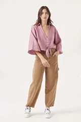 Camisa corta tipo crop en color rosado, con escote en V y cierre frontal con botones. Presenta mangas amplias de largo tres cuartos y un detalle de nudo ajustable en el bajo.