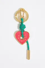 Llavero metálico dorado con mosquetón y anilla. Presenta un cordón de poliéster verde con detalles rojos y un nudo central, del cual cuelga un dije en forma de corazón rosado con el logo de la marca Bimba y Lola grabado en dorado.