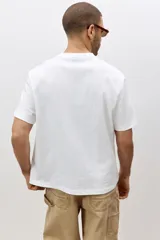 Remera blanca de algodón pesado, corte holgado, con cuello redondo ribeteado, hombros caídos y bajo recto.
